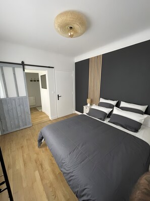 Een moderne slaapkamer met een groot bed, een houten vloer, een donker hoofdeinde en een plafondlamp.