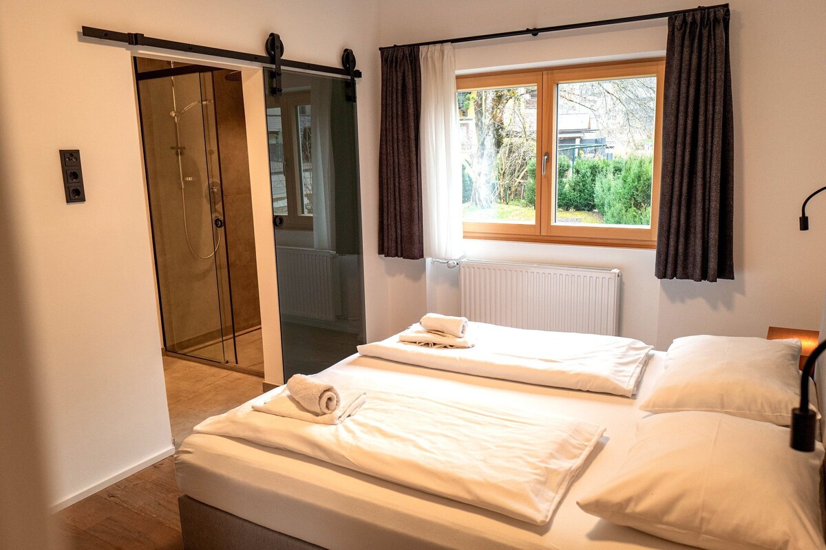Een slaapkamer met twee bedden, een schuifdeur naar een douchegedeelte, een raam met gordijnen en een radiator.