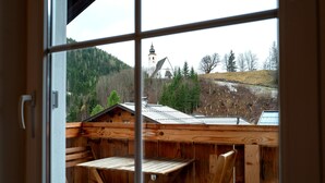 A wooden balcony with a view of a church and forested hills.