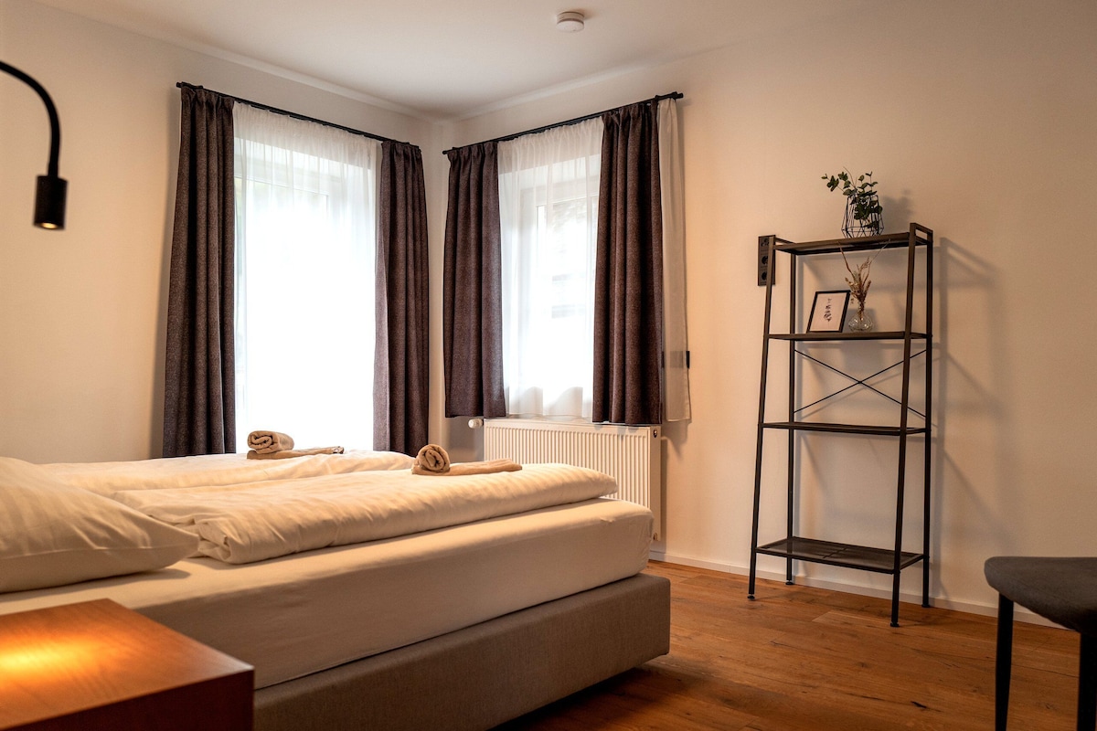 Een slaapkamer met een bed, een radiator, een plank met een plant en een raam met gordijnen.