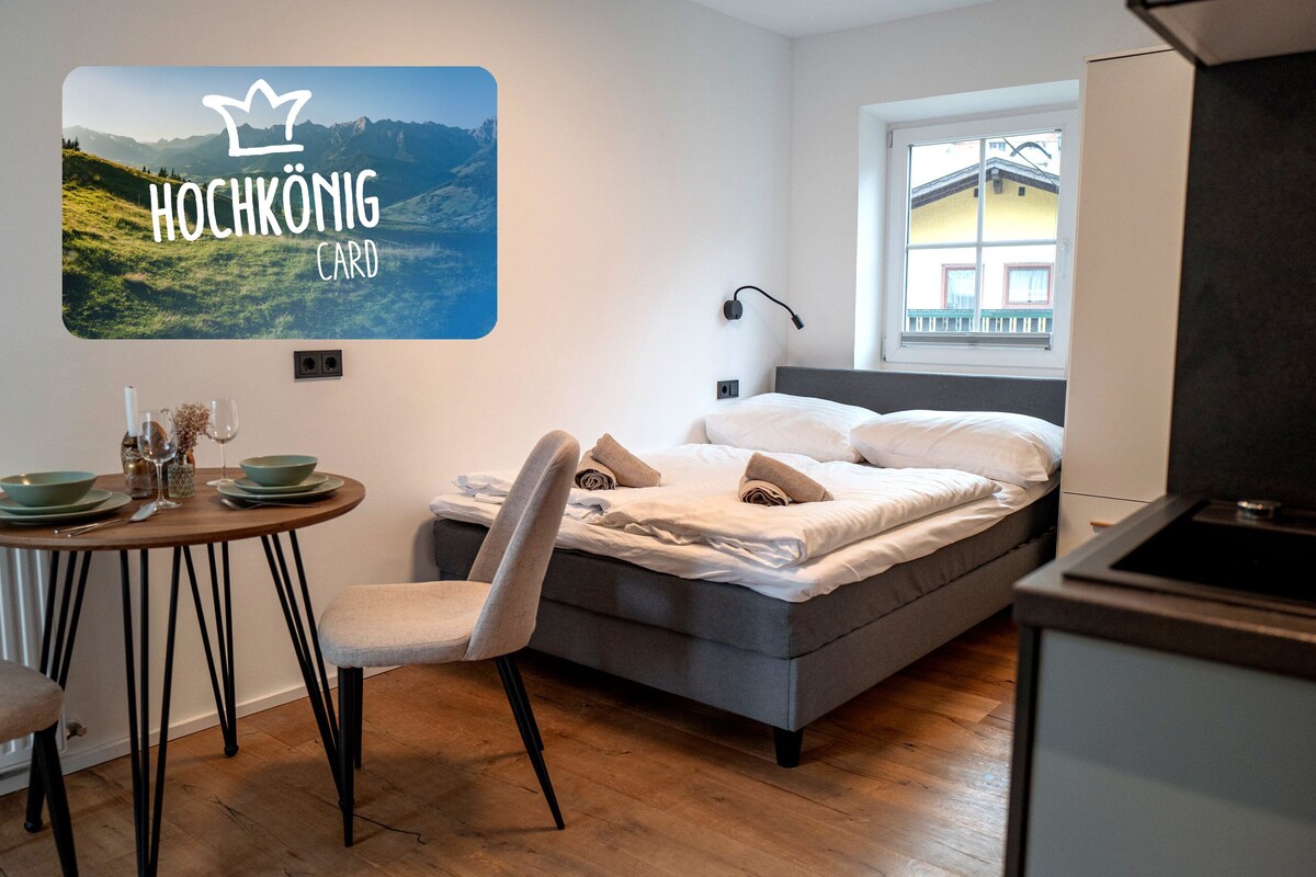 Een moderne hotelkamer met een bed, een bureau met stoel, een raam met uitzicht op bergen en een kaart bevestigd aan de muur.