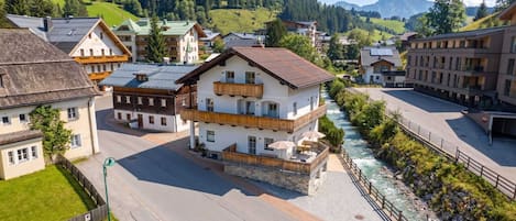 A multi-story building with balconies, a river running alongside, and a mountainous backdrop.