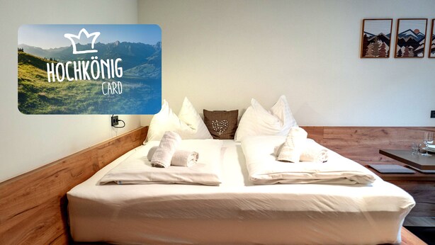 A hotel room with a wooden headboard, a bed with white linens, and a wall-mounted card displaying 'HOCHKÖNIG CARD'.