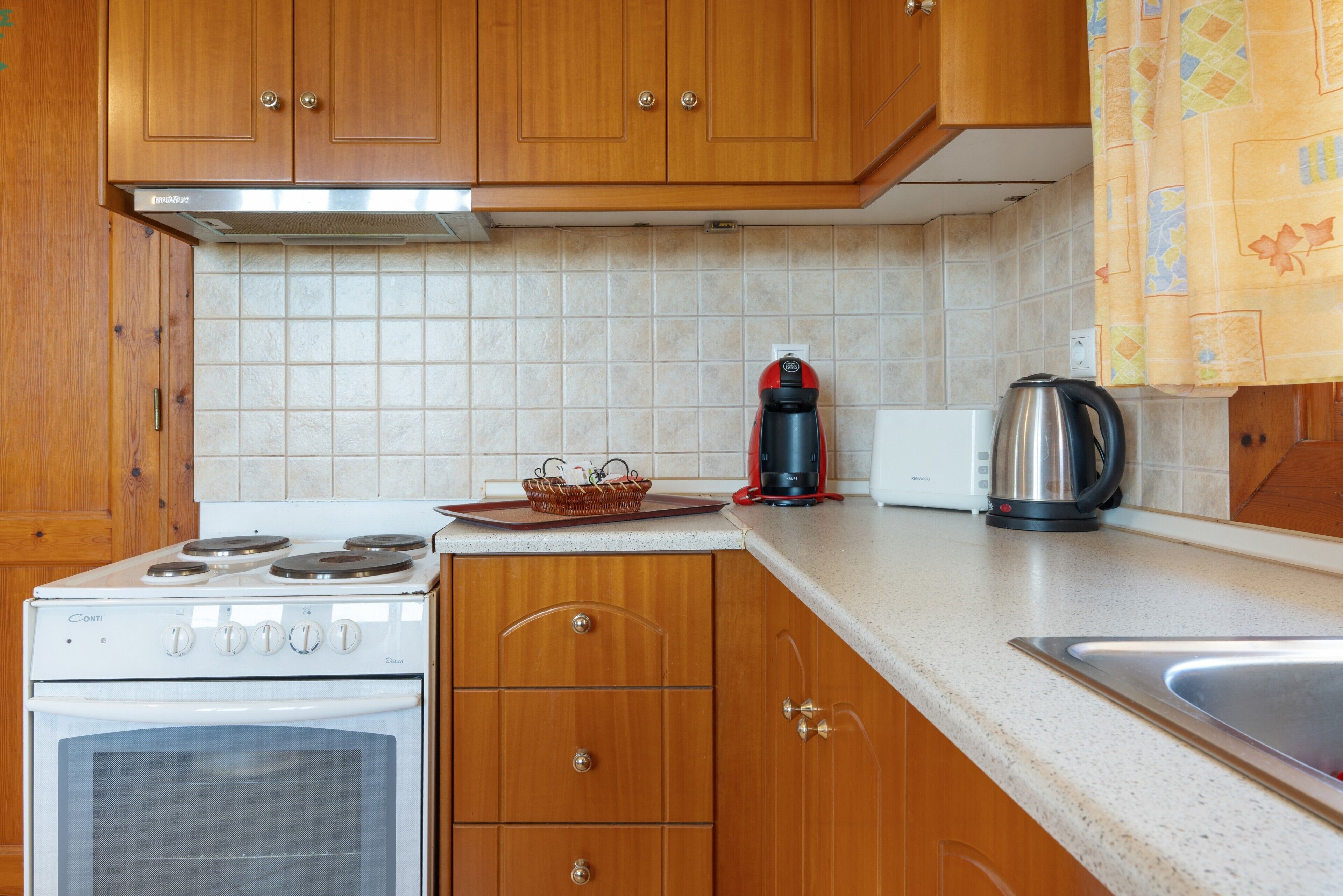 A kitchen with wooden cabinets, a white stove, a kettle, and a sink.