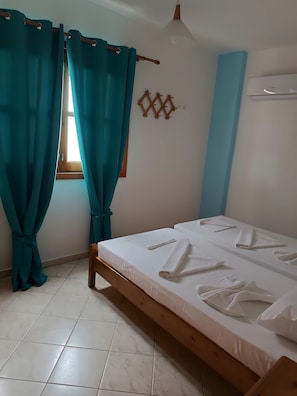 A bedroom with a bed, teal curtains, a window, and a wall-mounted air conditioner.