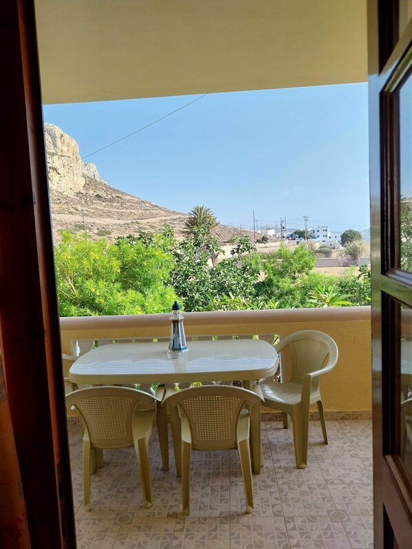 A balcony with a table and chairs, a view of a mountainous landscape, and a clear sky.