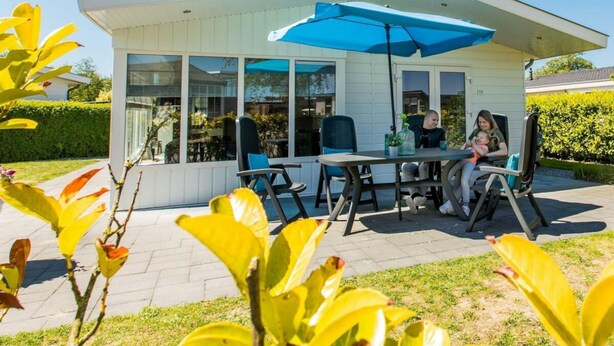 A modern outdoor patio with a table and chairs, a blue umbrella, and a white building with large windows. - Holiday Home in Noordwijk With Terrace (Noordwijk)