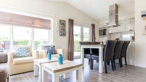 A modern living room with a sofa, a coffee table, and a dining area with chairs. - Holiday Home in Noordwijk With Terrace (Noordwijk)