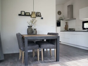 Ein moderner Essbereich mit einem Holztisch und grau gepolsterten Stühlen, einer Pendelleuchte und einer Vase mit Ästen.