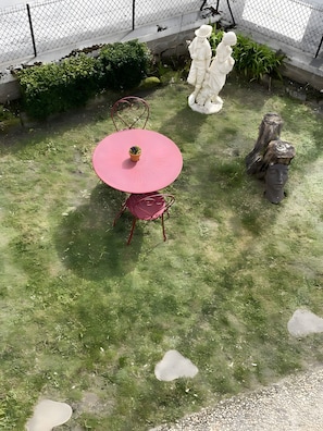 A fenced outdoor area with a pink metal table and chairs, a small potted plant, and a statue.