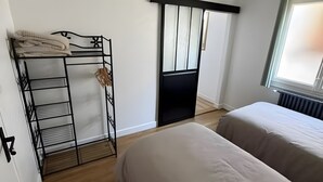 A bedroom with a bunk bed, a black metal shelf unit, a sliding door, and a large window.
