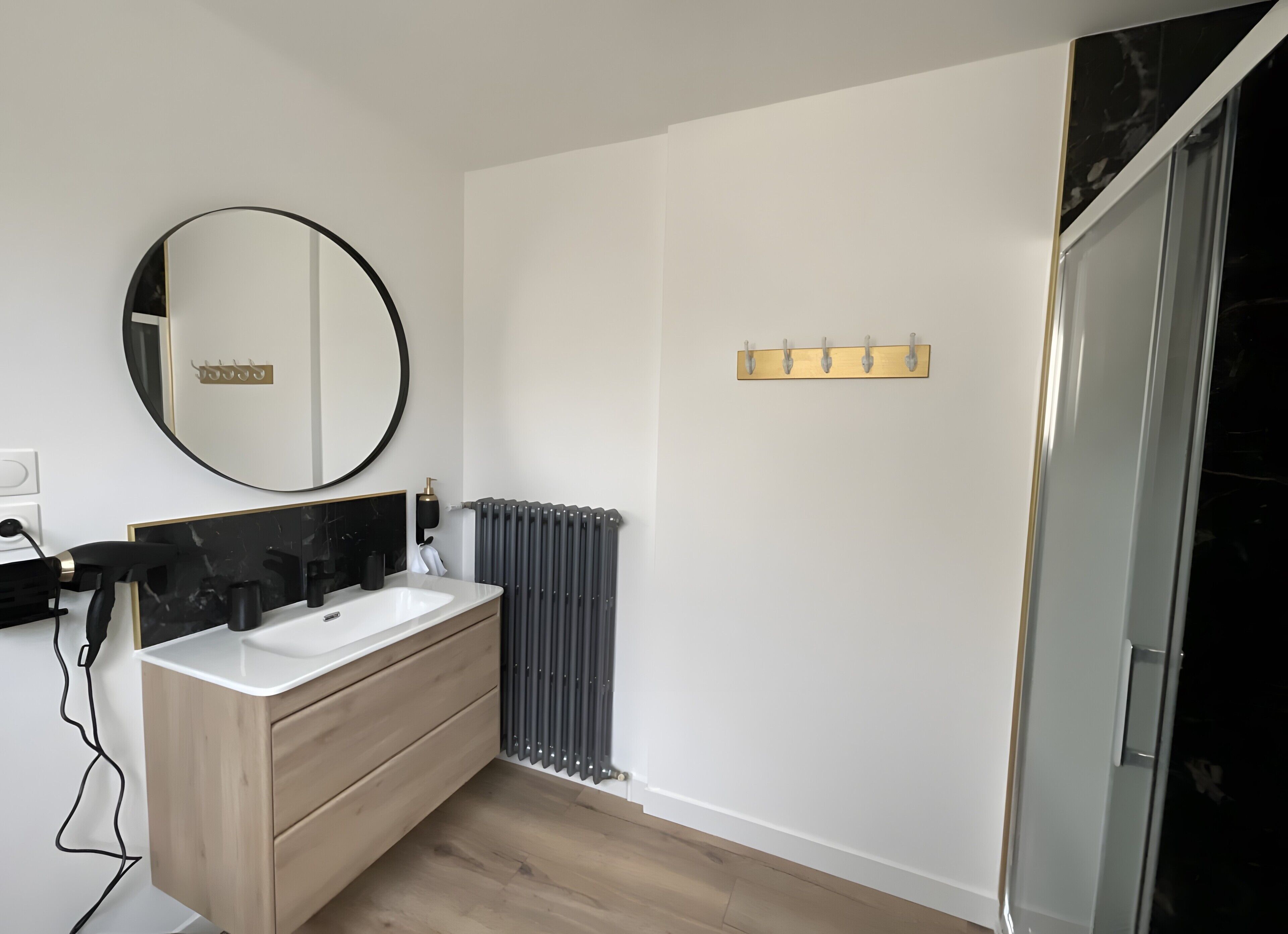 A bathroom with a round mirror, two sinks, a radiator, and a shower area.