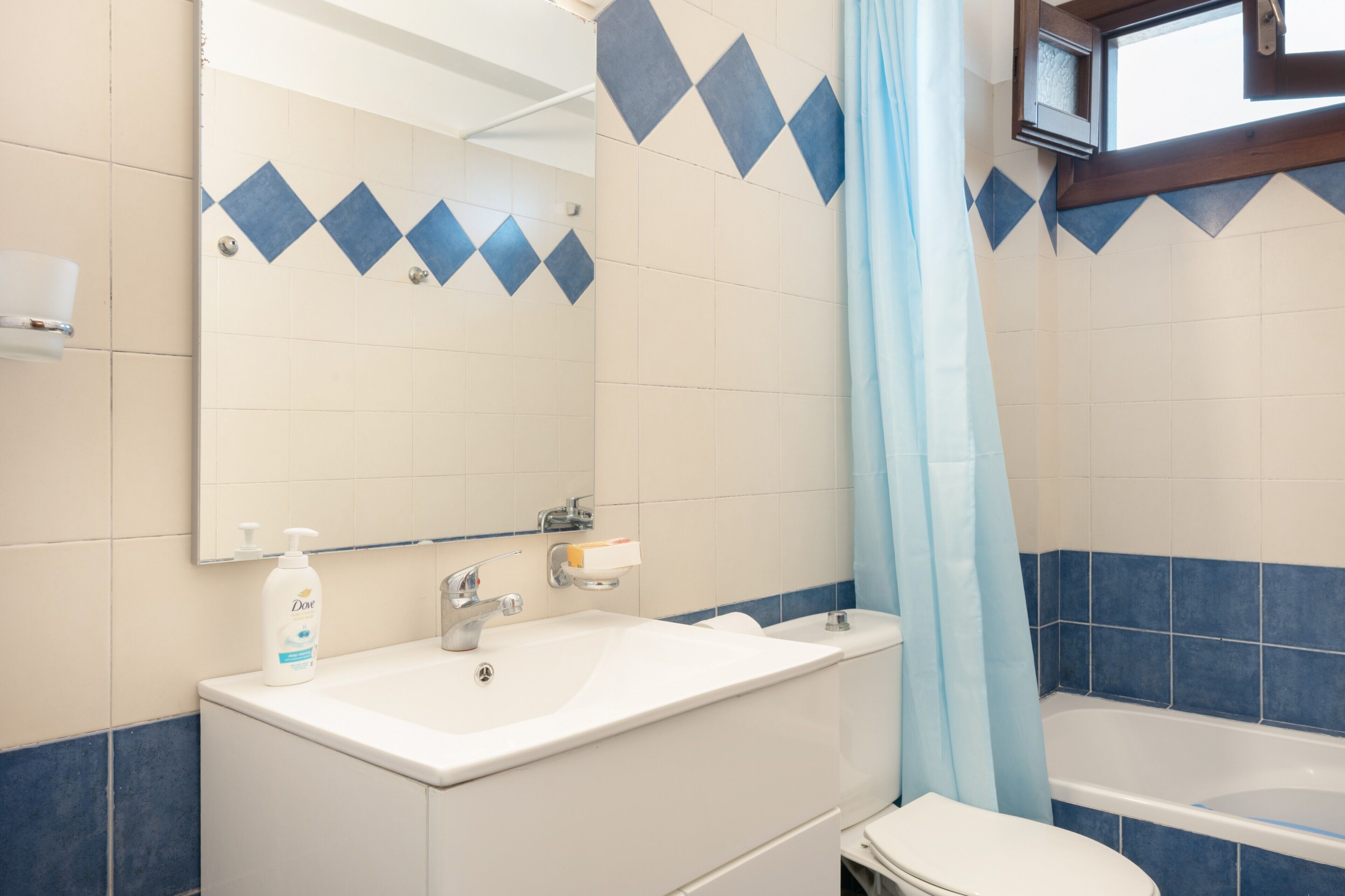 A bathroom with a white sink, a mirror, a shower curtain, and a bathtub.