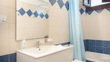 A bathroom with a white sink, a mirror, a shower curtain, and a bathtub.