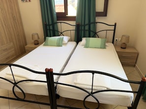 A double bed with a metal frame, two bedside tables with lamps, and green curtains.
