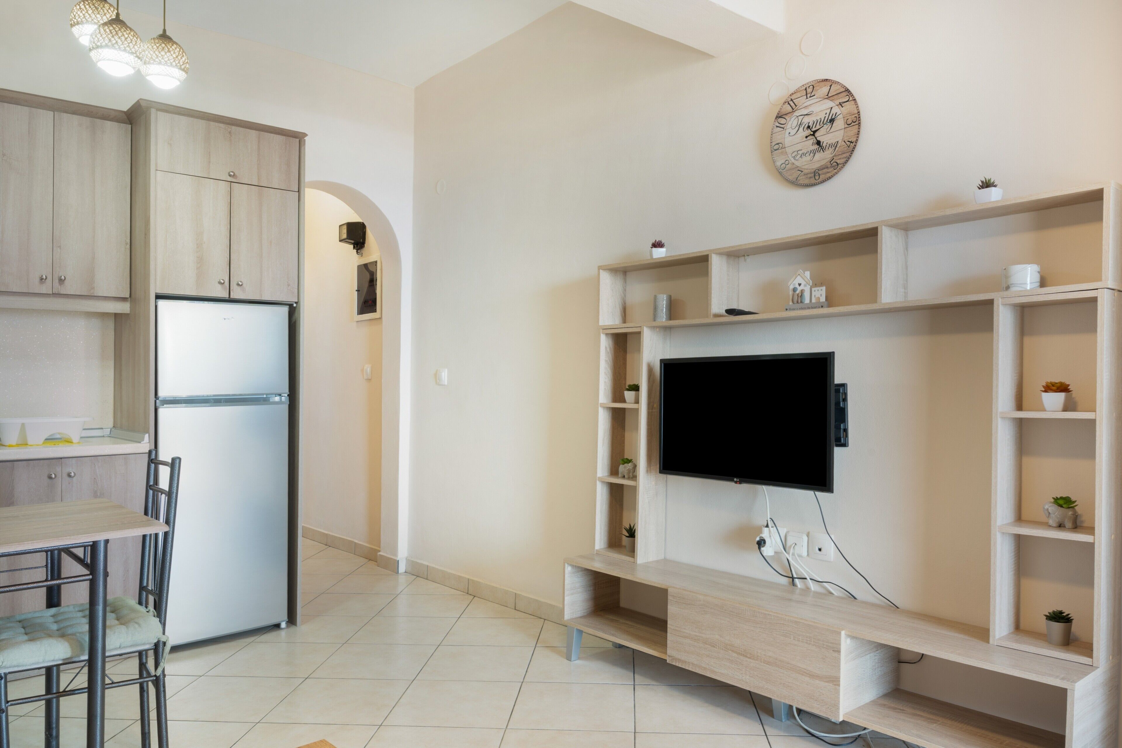 A modern kitchen with a built-in refrigerator, a dining area with chairs, and a TV mounted on a wooden shelf.