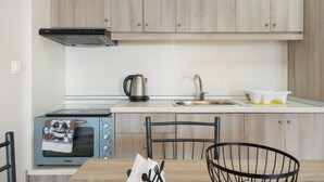 Una cocina compacta con horno integrado, hervidor, lavabo y una mesa de comedor con sillas.