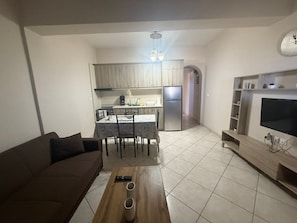 Un espace de vie compact comprenant un coin cuisine, un coin repas, un canapé, une table basse et un téléviseur.