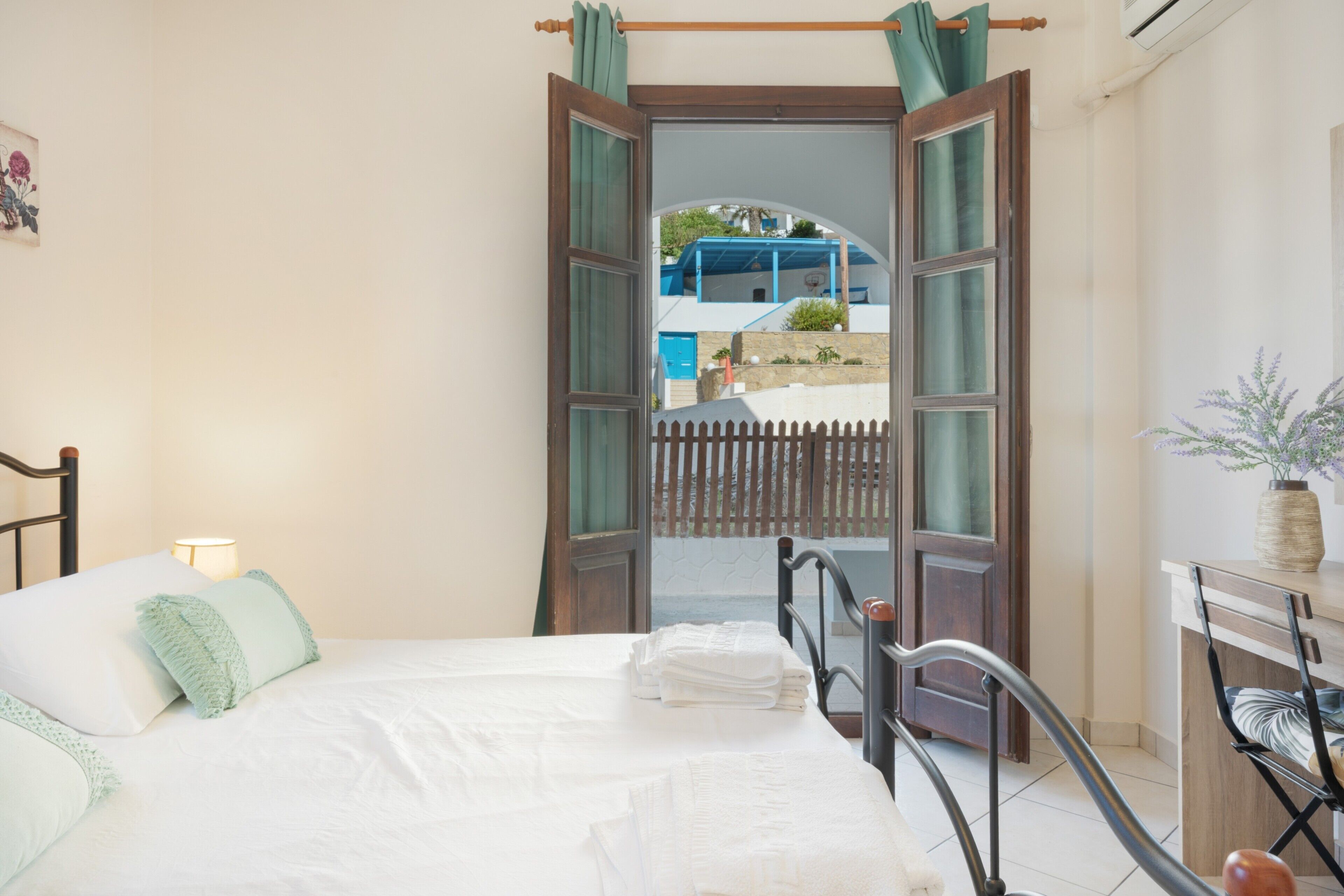 Un dormitorio con cama, mesita de noche, lámpara y vista al exterior.