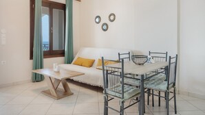 Una habitación con una mesa de comedor, sillas, un sofá con cojines, una ventana con cortinas y espejos montados en la pared.