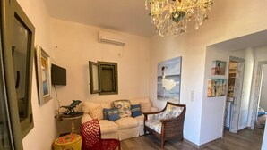 Uma sala de estar com sofá, uma poltrona vermelha, um lustre e um quadro na parede.