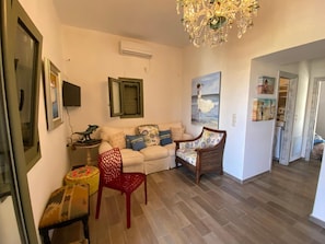 A living room with a sofa, a red chair, a chandelier, and a painting on the wall.