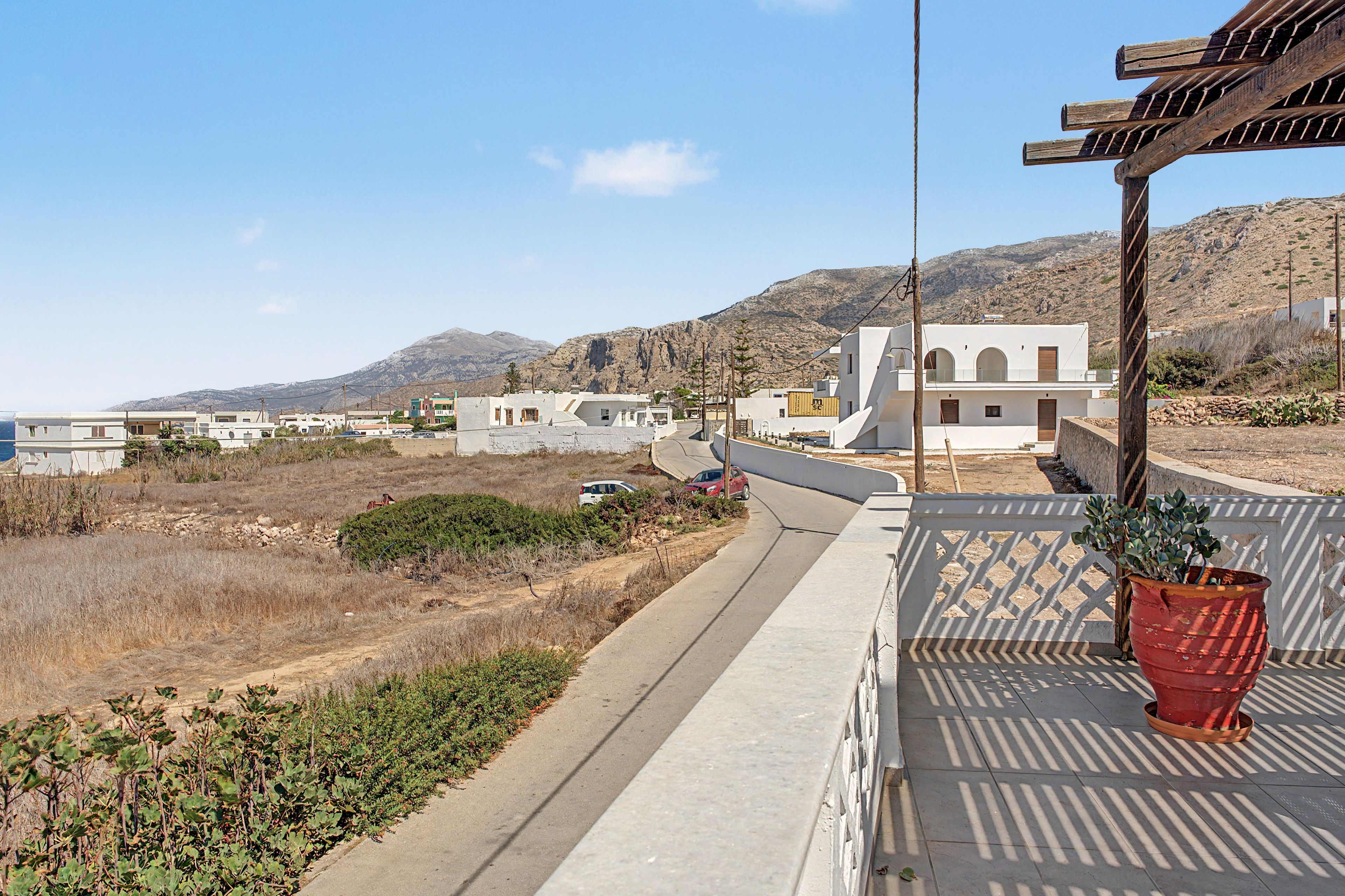 Una zona residenziale costiera con edifici bianchi, una strada asfaltata e montagne sullo sfondo.