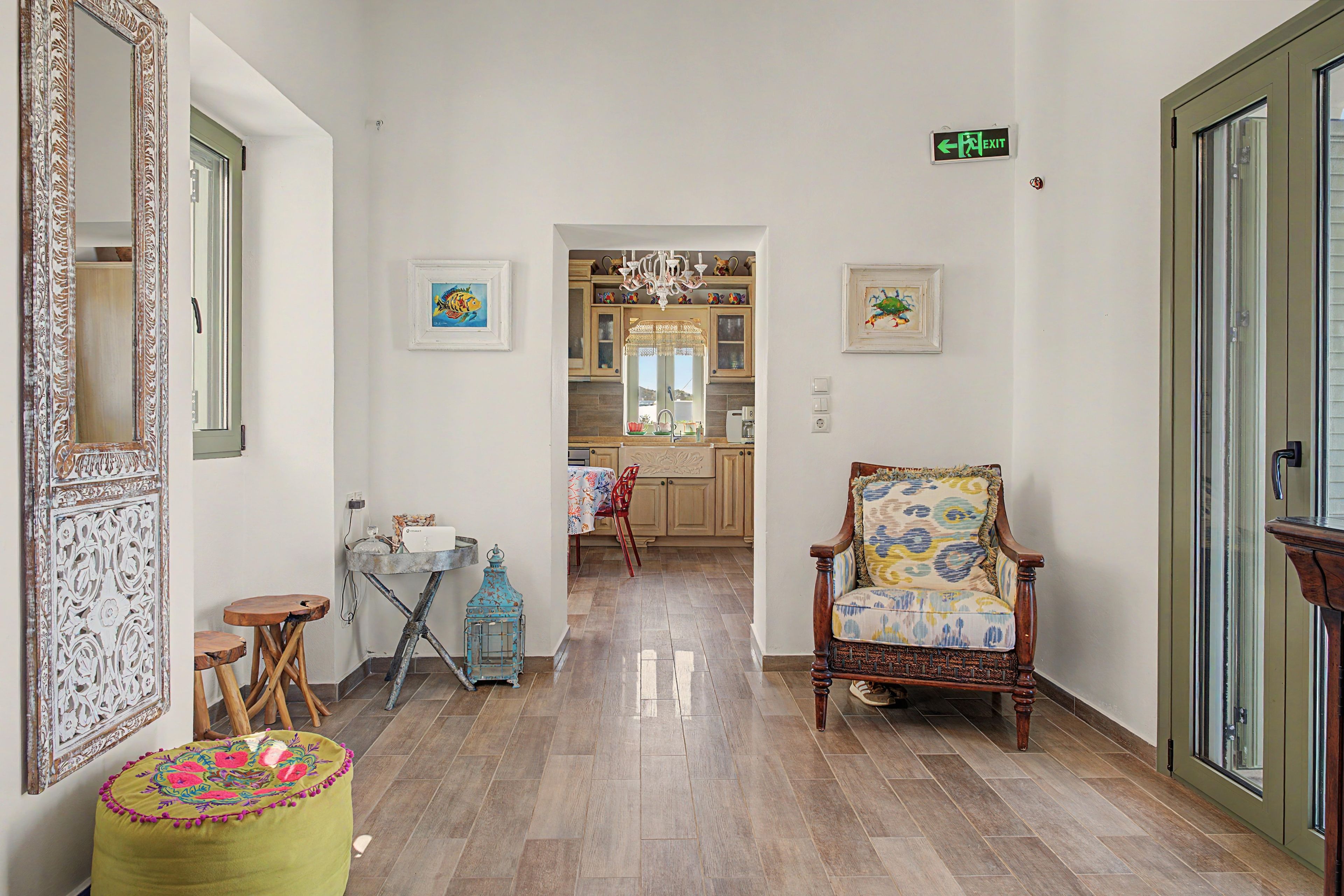 Un couloir doté d’un plancher en bois, une chaise avec un coussin à motifs, une petite table sur laquelle est posé un vase, et un miroir avec un cadre décoratif.