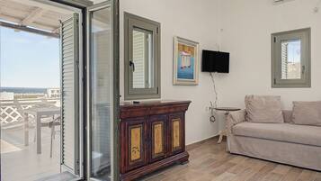 Una stanza con una porta finestra scorrevole che dà su un balcone, un armadio in legno, una TV a schermo piatto fissata al muro e un divano color beige.