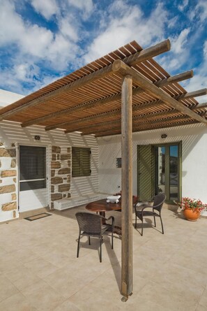 A covered patio area with a table and chairs, stone walls, and a wooden pergola.