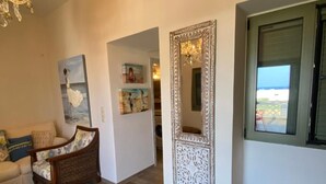 Uma sala de estar com sofá, uma cadeira de vime, um banquinho pequeno, um espelho decorativo e um quadro na parede.