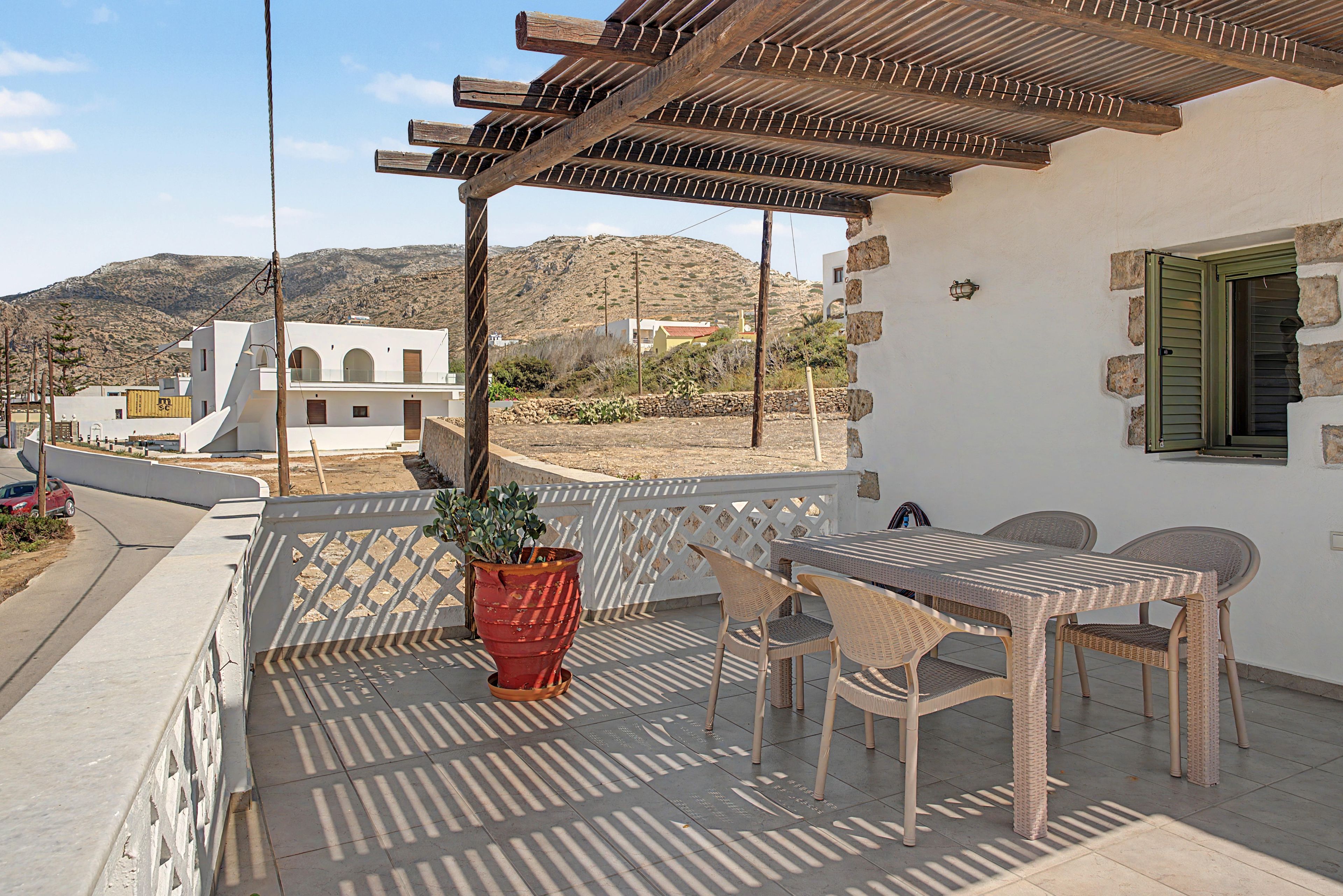 Un balcón con una mesa, sillas, una planta en maceta y vistas a un paisaje montañoso.
