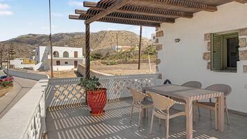 Un balcón con una mesa, sillas, una planta en maceta y vistas a un paisaje montañoso.