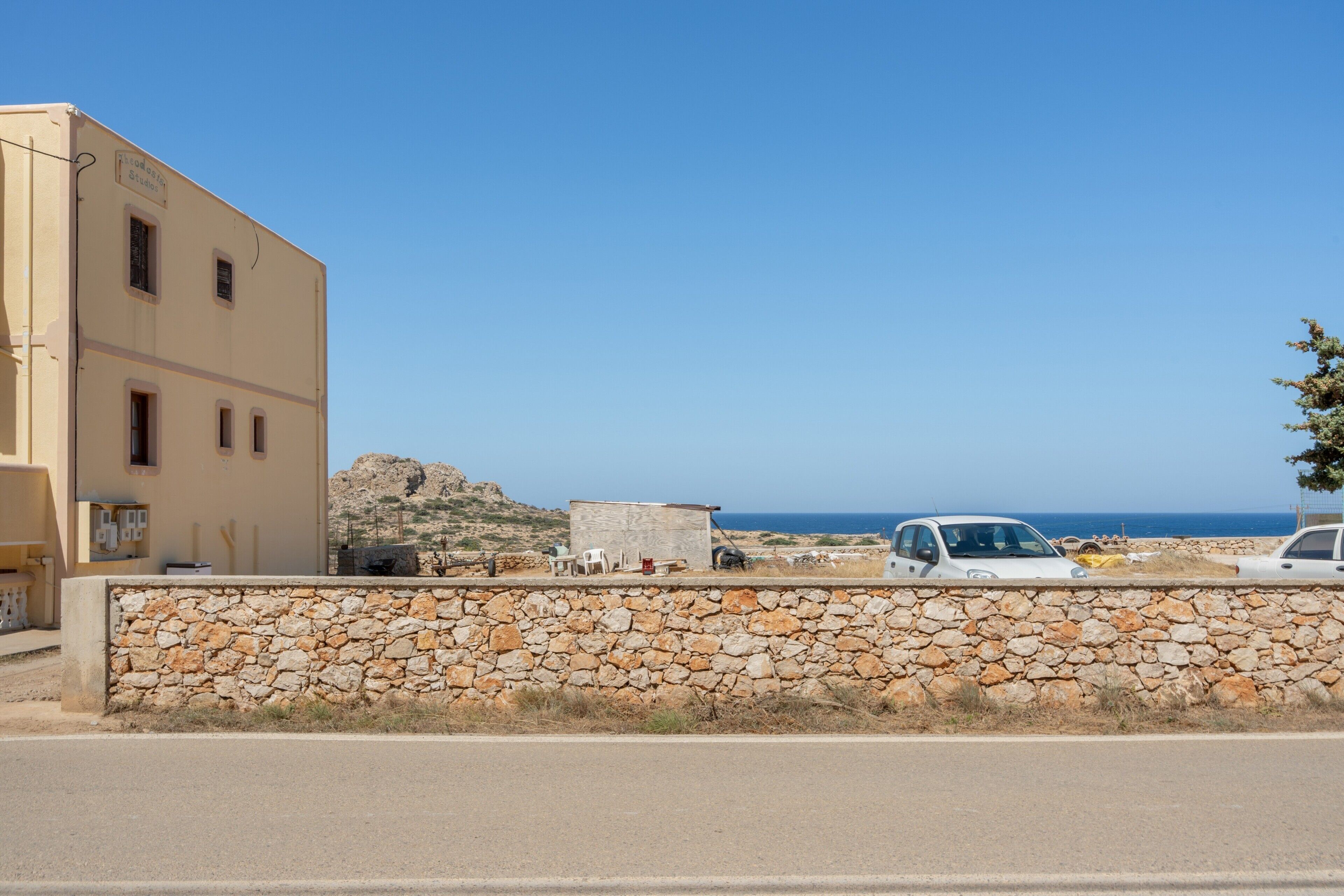 Un bâtiment situé sur la côte, avec un mur de pierre à l’avant, une voiture garée et une vue dégagée sur la mer.