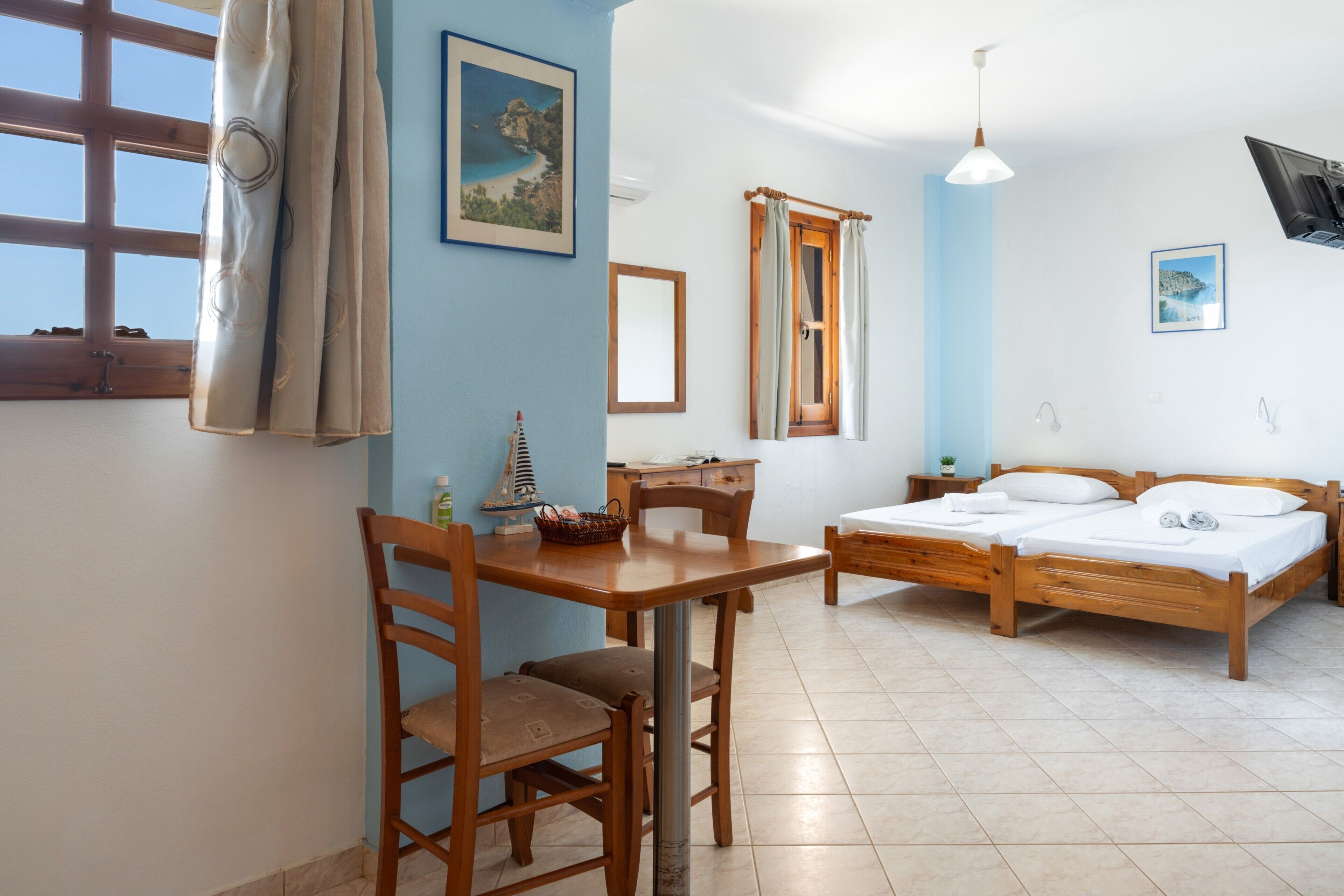 Une pièce avec un lit en bois, une table en bois avec des chaises, un bureau et une fenêtre avec des rideaux.