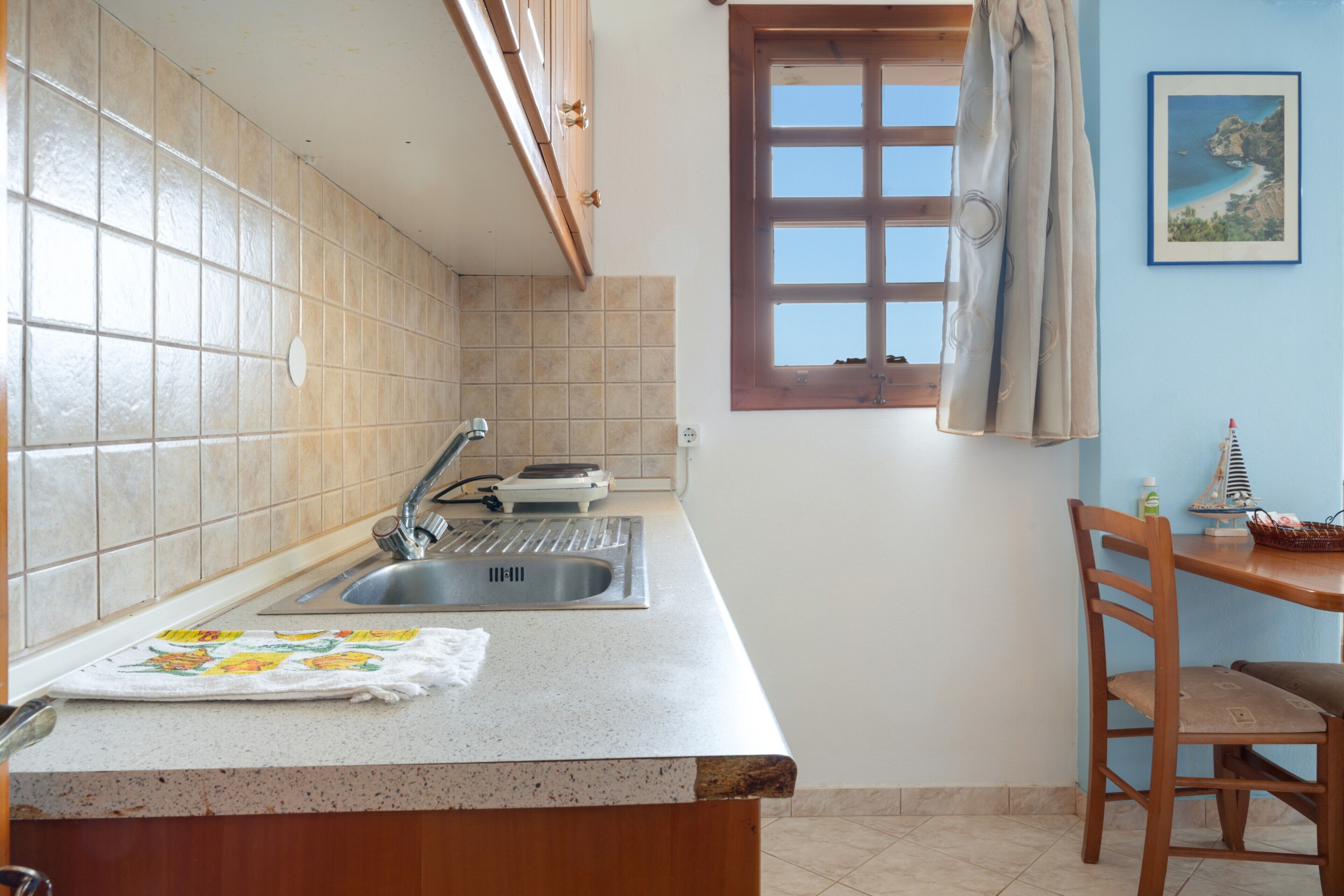 A kitchen with a sink, a window with curtains, a dining table with chairs, and a small decorative item on the table.