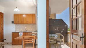 Una cocina con armarios de madera, una mesa de comedor con sillas y un balcón con puerta.
