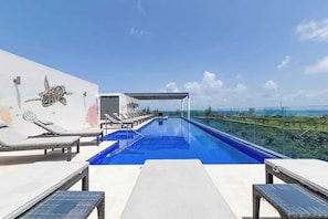Ein Rooftop-Pool mit Infinity-Kante, Liegestühlen, einer Pergola und einem Wandgemälde eines Meeresschildkröten.
