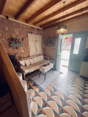 Una habitación acogedora con pared de piedra, techo de madera, sofá, una mesita y suelo con diseño.