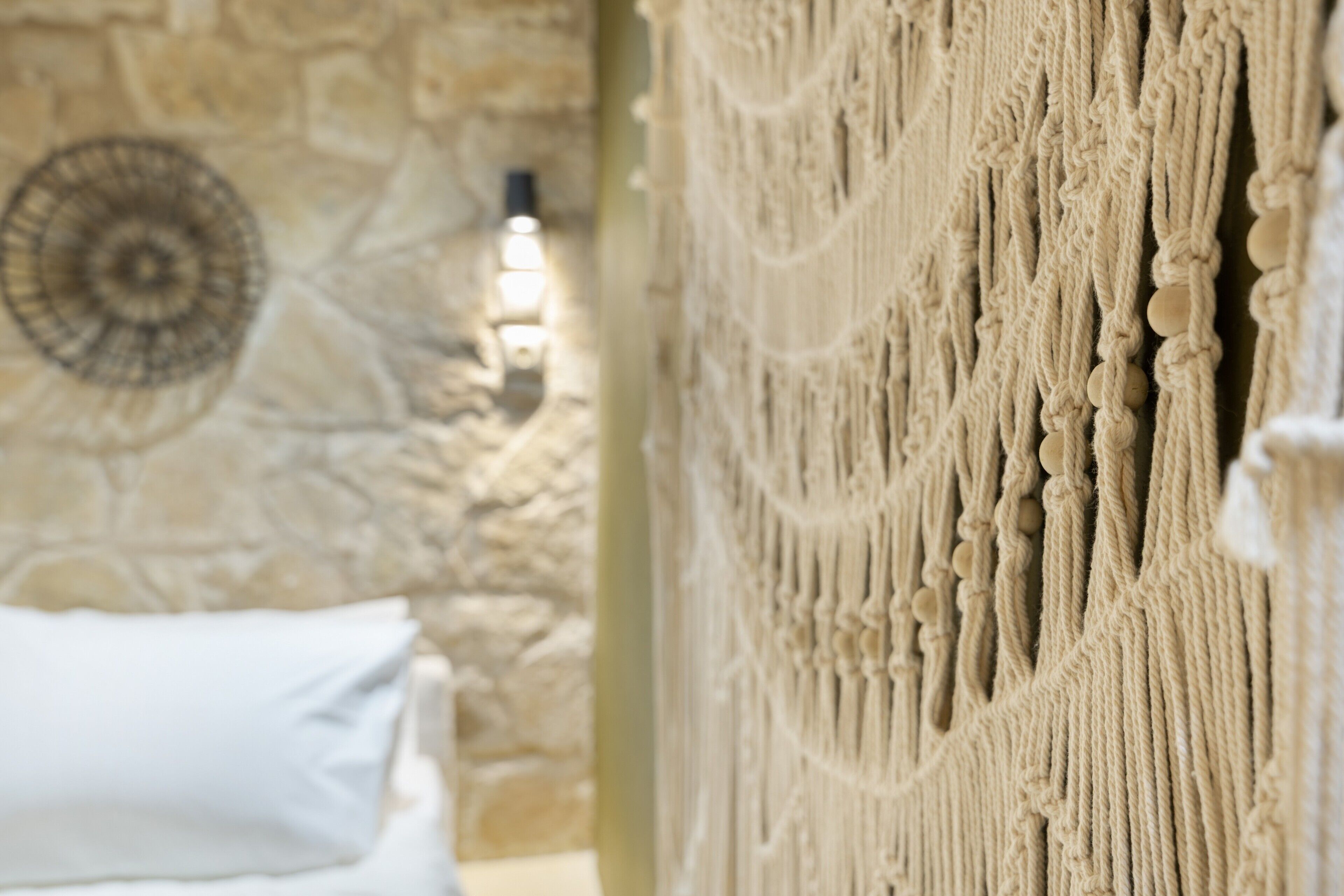 A room with a stone wall, a macrame wall hanging, and a white pillow.