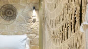 A room with a stone wall, a macrame wall hanging, and a white pillow.