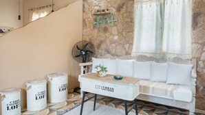 Ett rum i loftstil med en vägg av natursten, en vit soffa, ett träbord och en fläkt.