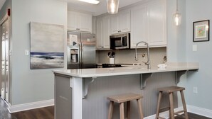 A modern kitchen with white cabinetry, a central island with stools, stainless appliances, and pendant lighting. - ☀️ Short Walk to Beach - Summerhouse 206 – Brown Eyed Girl ☀️ (Mexico Beach)