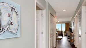 A hallway with a painting, white doors, a ceiling fan, and a view to a living area. - ☀️ Short Walk to Beach - Summerhouse 206 – Brown Eyed Girl ☀️ (Mexico Beach)