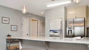 A modern kitchen with a stainless steel refrigerator, a white countertop, and a hanging light fixture. - ☀️ Short Walk to Beach - Summerhouse 206 – Brown Eyed Girl ☀️ (Mexico Beach)