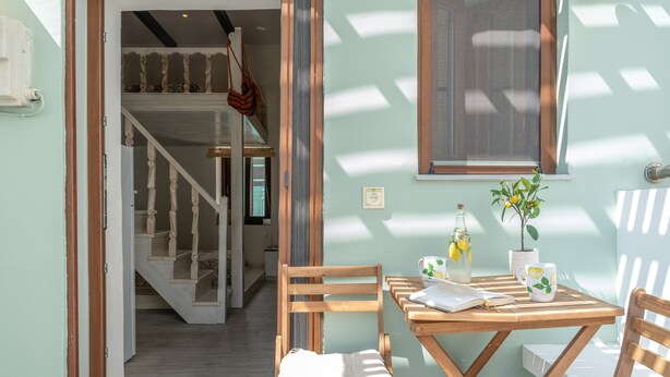 Ein Zimmer mit Holztisch, Stühlen, einer Treppe und einem Fenster mit Pflanze.