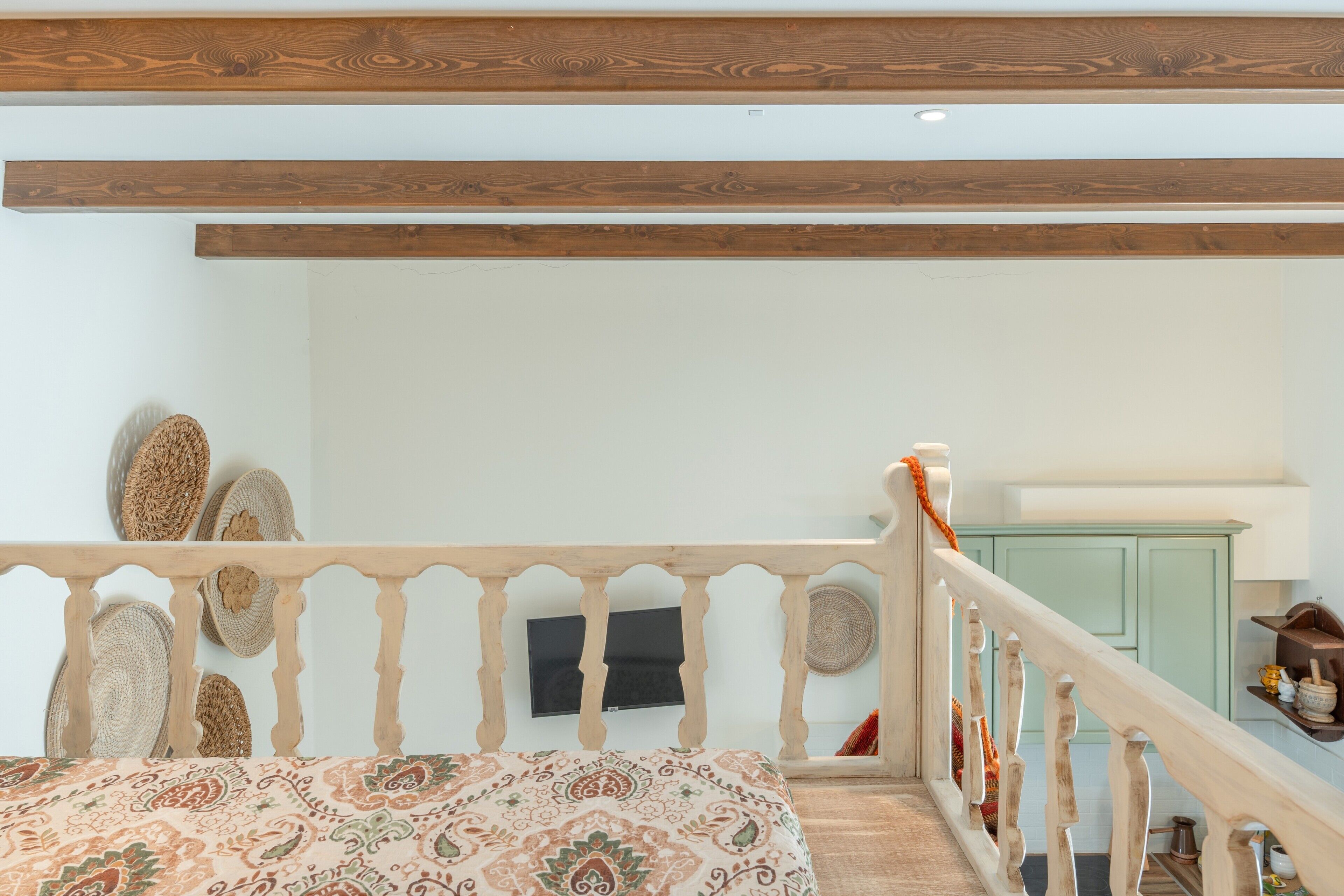 Een slaapkamer met een bedovertrek met dessin, een houten plafond, een witte muur en een groen kastje.
