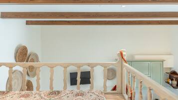 Een slaapkamer met een bedovertrek met dessin, een houten plafond, een witte muur en een groen kastje.