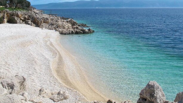 A coastal beach with clear water, rocky shoreline, and distant mountains. - Ester Premium Stay (Krsan)