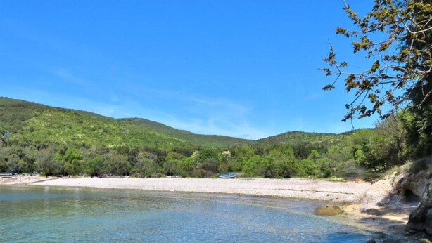 A clear lake with a rocky shoreline, surrounded by green hills and sparse vegetation.